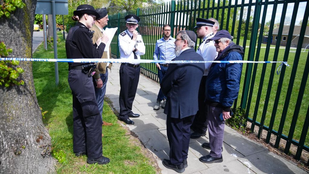 Rabbi Yehuda Black (centre) identifies himself to a police officer as he enters the restricted zone outside the Kenton United Synagogue in Harrow