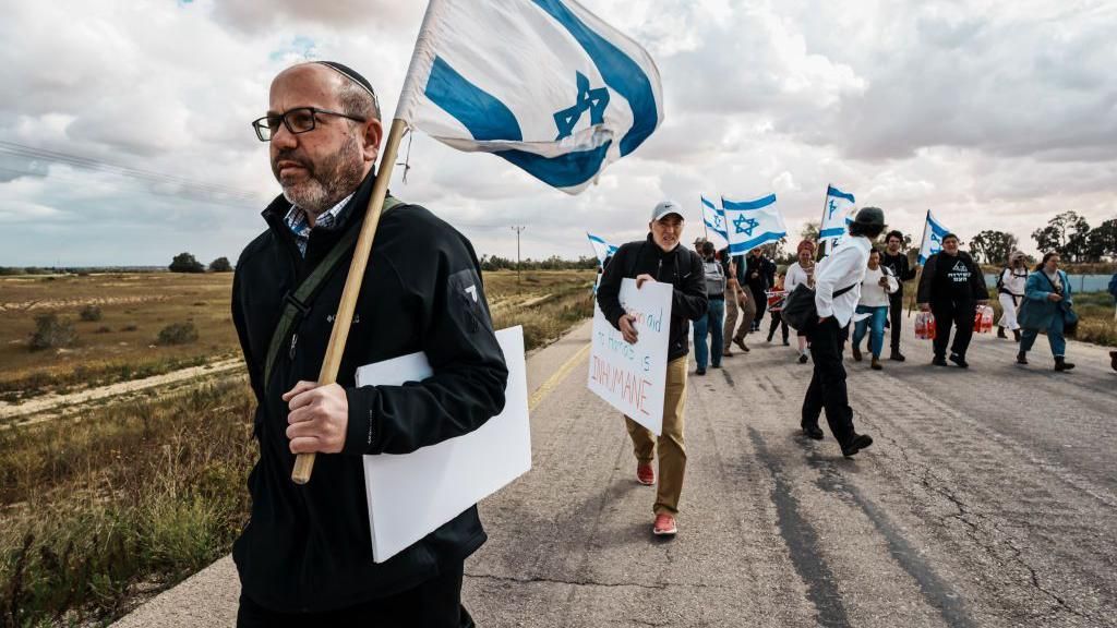 Tzvika Mor lead protesters from the Tsav 9, or known as Order 9, on a march towards the border crossing checkpoint with the goal of blocking aid shipments from getting into the Gaza, in Kerem Shalom, Israel, Thursday, March 7, 2024. The protests to halt aid delivery into Gaza were started by religious Zionists, but now draw many secular participants.