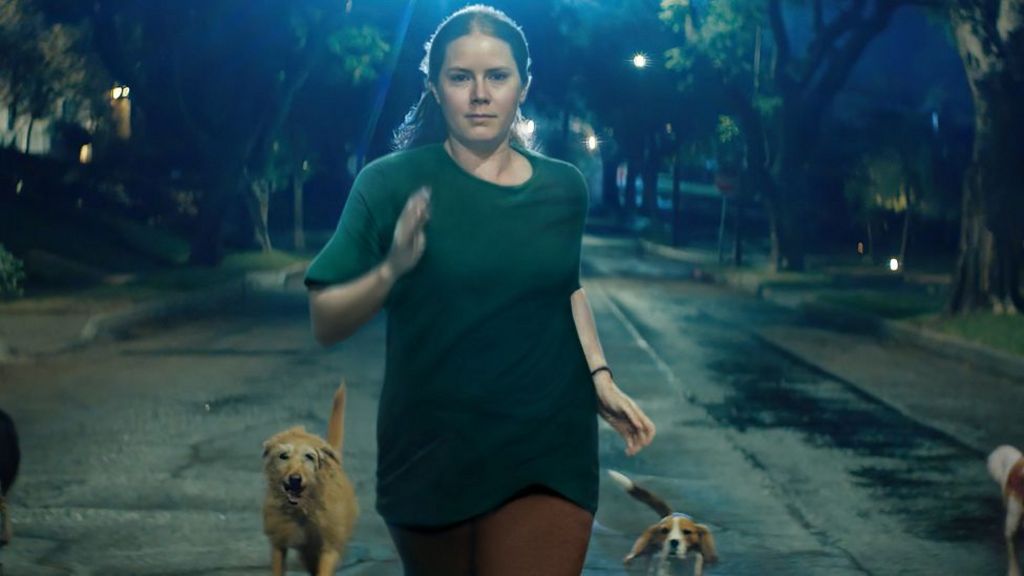 Amy Adams in Nightbitch, seen running down the street surrounded by dogs