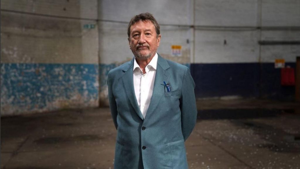 Peaky Blinders creator Steven Knight in a blue suit and a white shirt standing in an empty warehouse