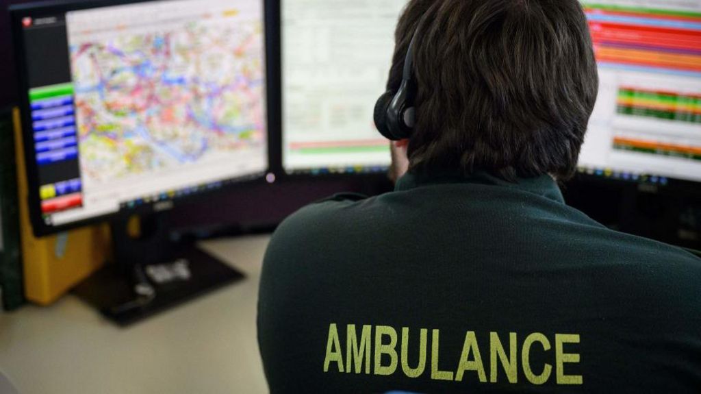 An emergency services call handler sitting at a desk with a headset on taking a call