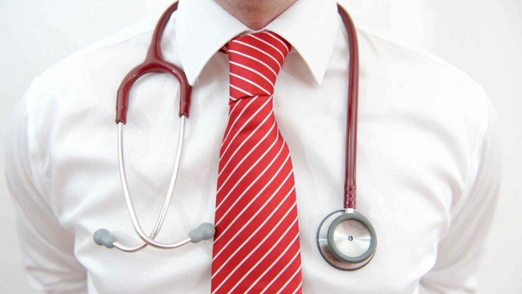 A stethoscope is draped over the shoulders of a person in a white shirt and wearing a red and white striped tie