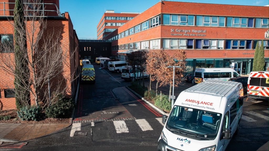 Several ambulances are parked outside St George’s Hospital in Tooting, South London. The large red-brick building has multiple windows and a sign reading ‘Grosvenor Wing Main Entrance’ above the entrance.