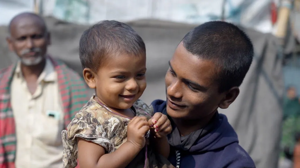 Rithick, Dipu's youngest brother, cradles 18-month-old Meghna outside their home in Mymensingh