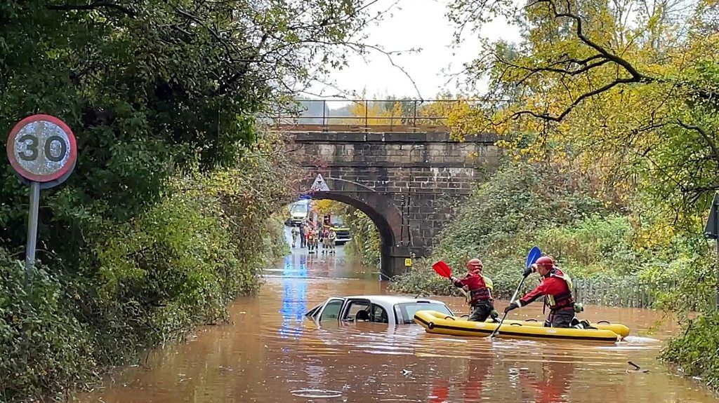 Car stranded under a bridge with rescuers using a canoe