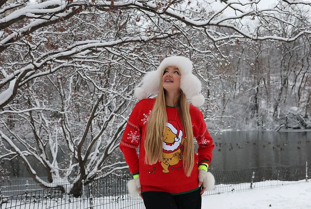 A person wearing a red Christmas-themed jumper looks at the snow in Central Park, New York City