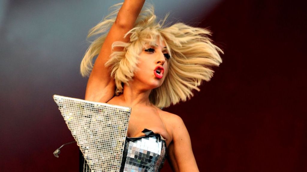Lady Gaga on stage with one arm in the air in an elaborate mirrored dress at Glastonbury in 2009