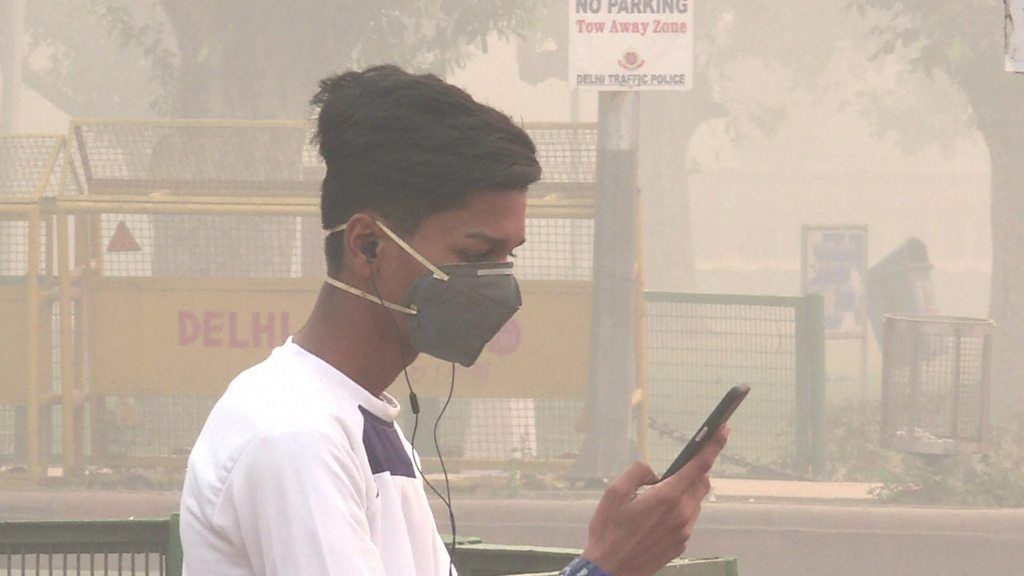 A young man wearing a breathing mask looks at his phone.