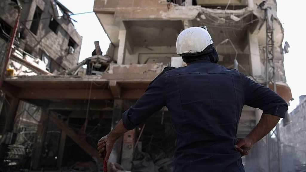 A member of the Syrian civil defence volunteers, known as the White Helmets, looks at a destroyed building following a reported air strike on the rebel-held town of Douma, on the eastern outskirts of the capital Damascus