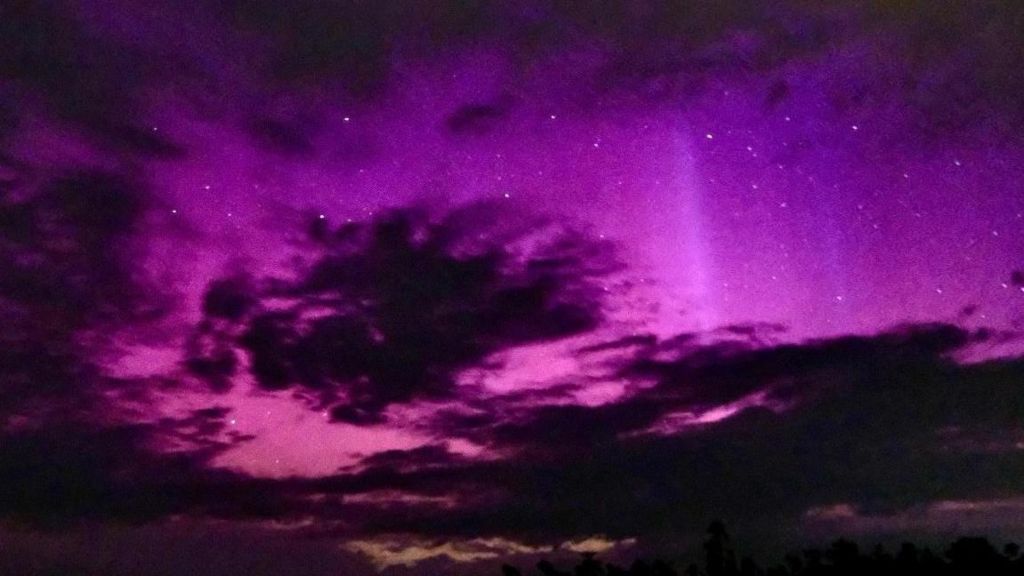 silhoutte of clouds in the night sky but behind the bright lights of the aurora glowing pink and purple