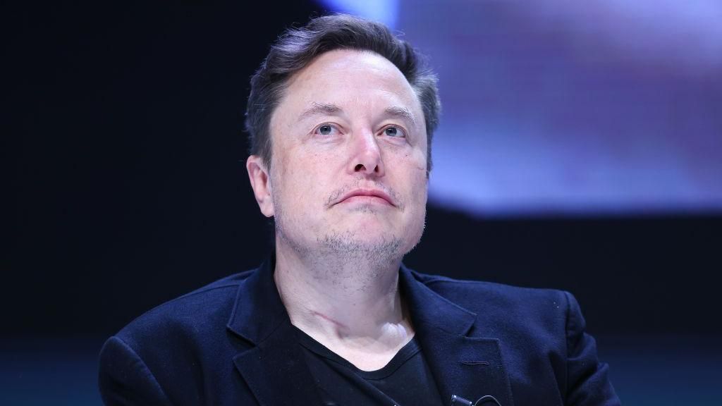 Tech entrepreneur Elon Musk wears a black blazer and T-shirt while answering questions at a conference