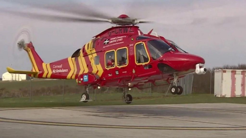Cornwall Air Ambulance seen taking off, with mainly red and some yellow in its design