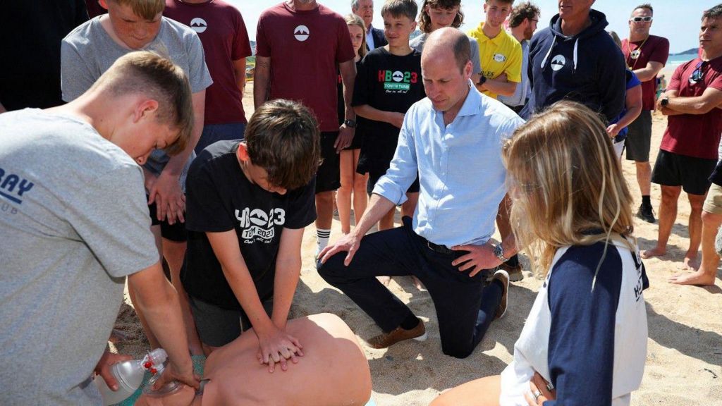 Prince William looks on as young lifeguards practice cardiopulmonary resuscitation on a mannequin
