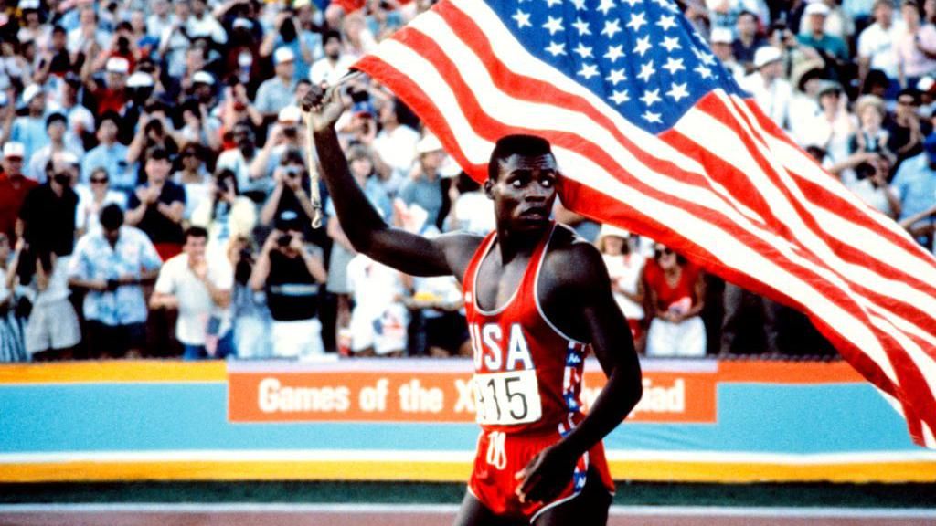 Carl Lewis holds a US flag on the athletics track