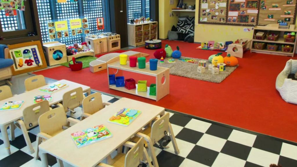 Black and white checkered floor next to red carpet with small wooden table and chairs and children's books and toys upon it