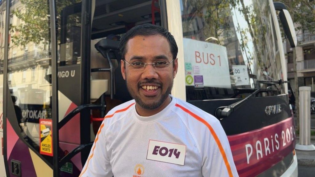 Mohammed stood in front of a Paris 2024 bus in a white top