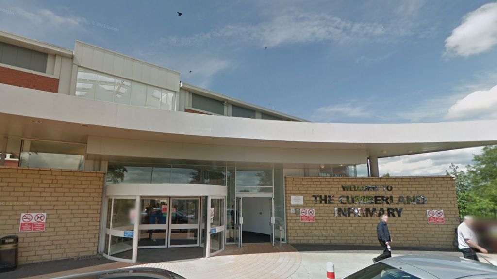 The hospital is a light brown coloured brick building with a metal sign saying 'Welcome to The Cumberland Infirmary'.