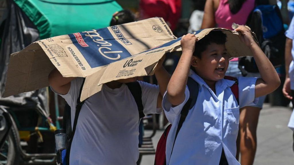 Students in the Philippines' capital city Manila use a cardboard to protect themselves from the sun