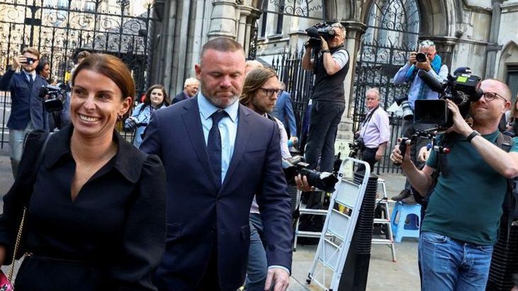 Coleen Rooney and her husband Wayne arriving in suits at the High Court, with lots of photographers taking pictures of them