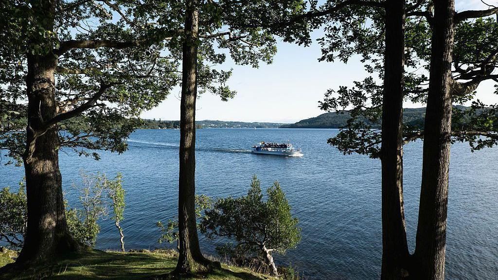 A general view of Windermere with trees on the lakeside and a boat on the water
