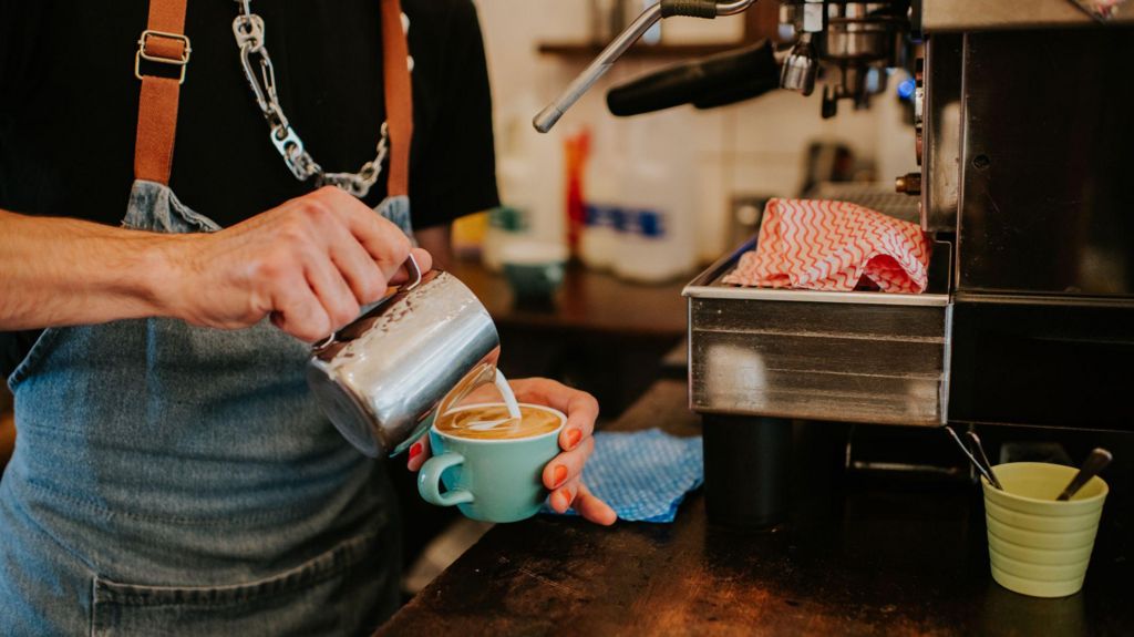 A stock photo of someone pouring milk into a coffee cup