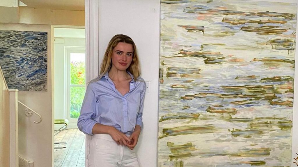 Genevieve de Vorms leaning against a wall with a green, blue and cream canvas to her left