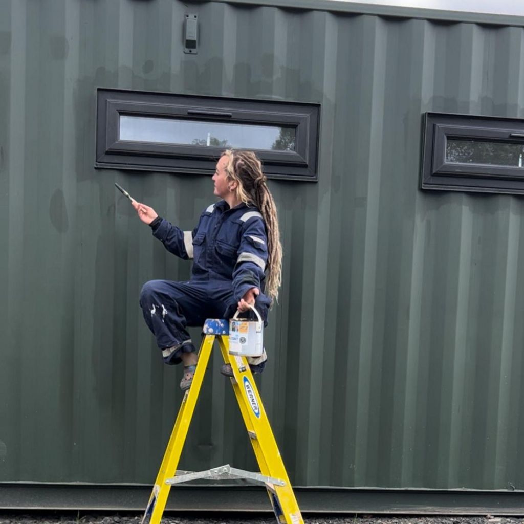 Woman sitting on a ladder painting a shipping container