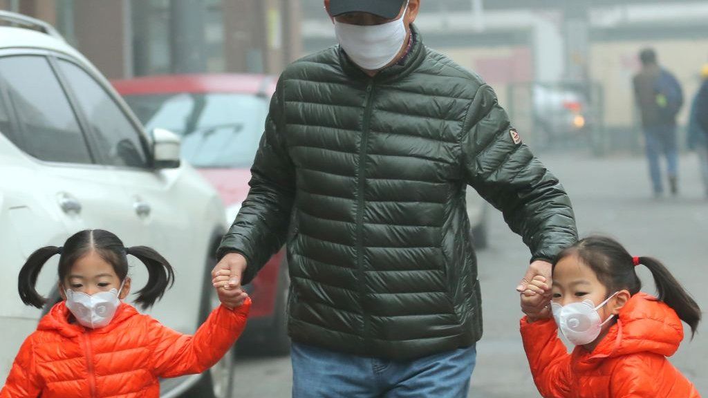 A man walks with two small girls through Beijing, with all three wearing face masks to protect against air pollution