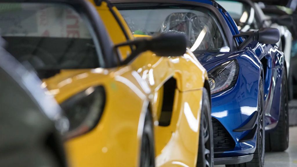 A row of cars parked in a line. They all are the same model of Lotus and are different colours, including bright yellow and blue. The picture is taken from the front of the cars.