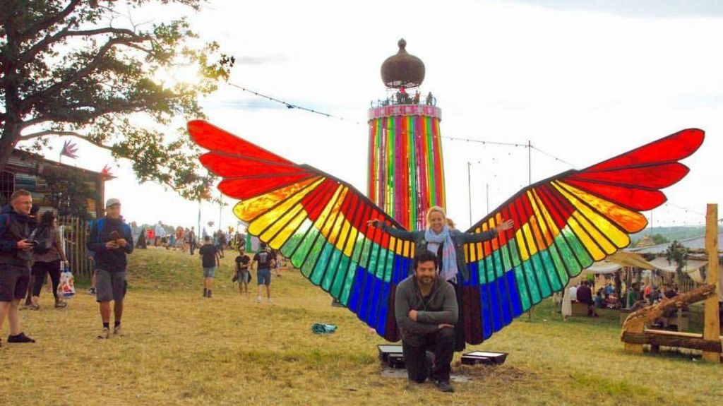 Emily Eavis and Edgar Phillips standing in front of the large stained glass wings at the festival
