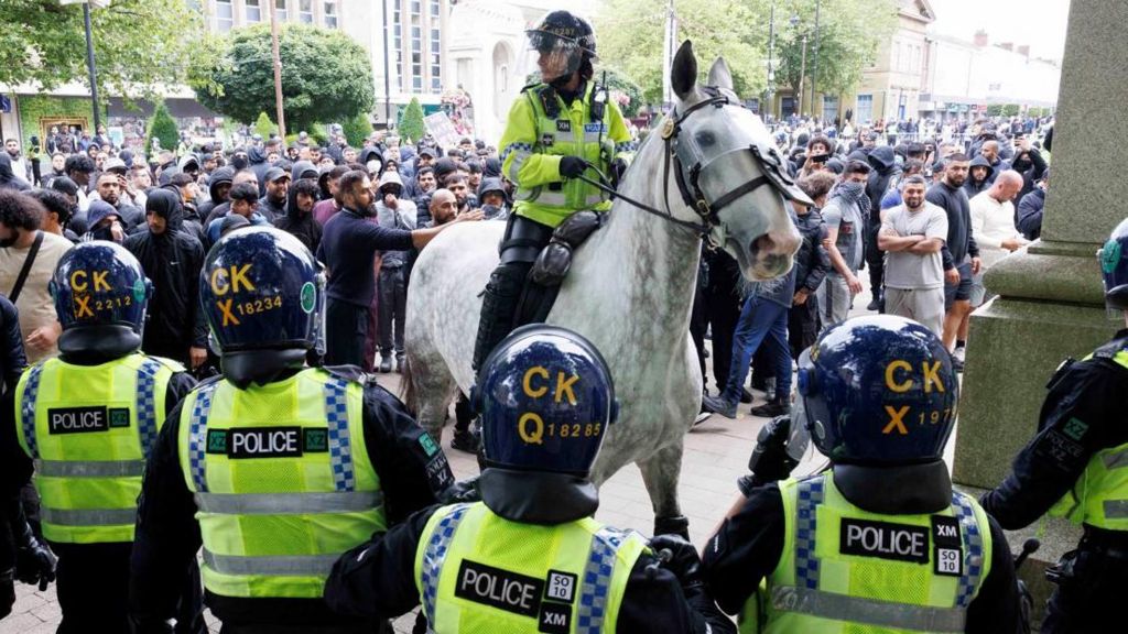 Police officers stand guard next to counter-protesters, on the day of a protest against illegal immigration, in Bolton, Britain,