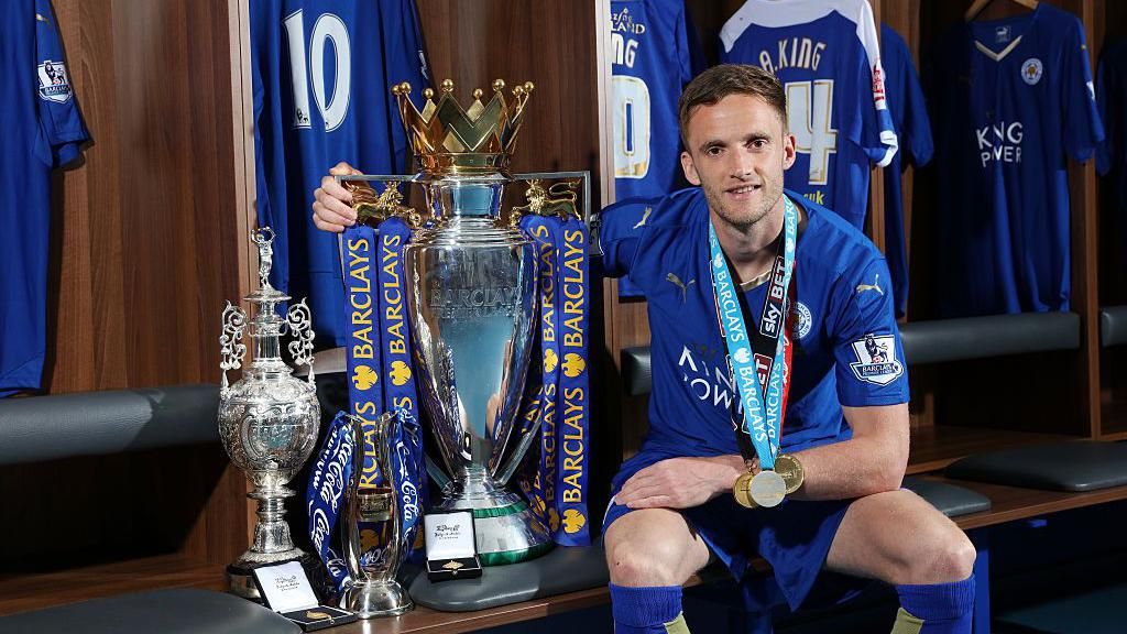 Andy King sits with the League One, Championship and Premier League trophies