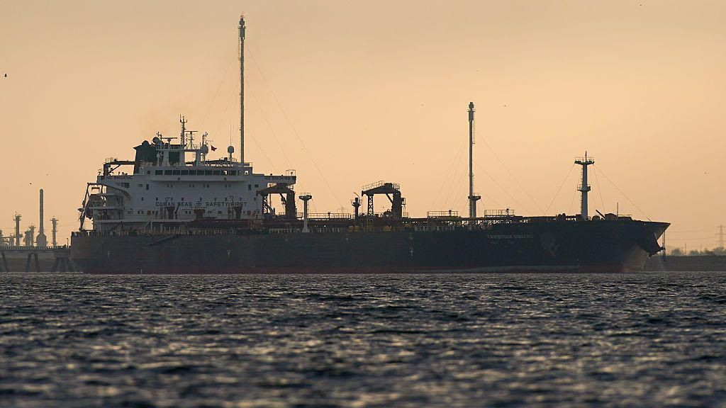 An oil tanker at sea silhouetted against a sky at sunset.