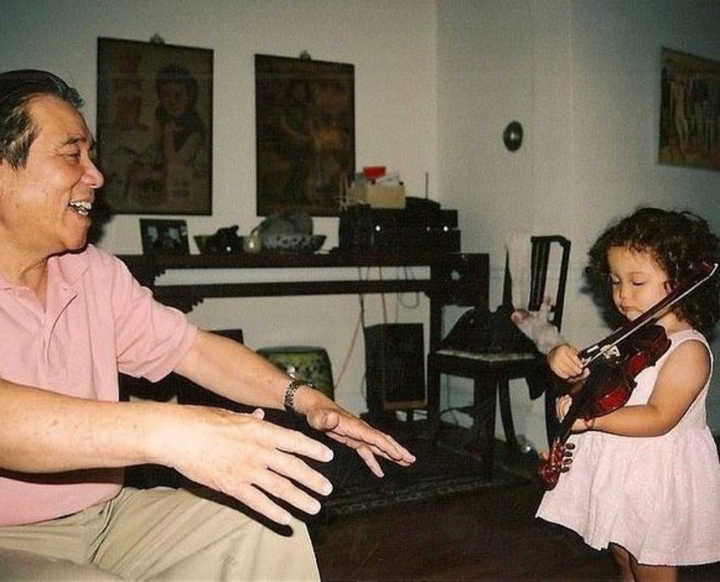 A childhood photo of Laufey shows her at home in Iceland, playing violin while her grandfather looks on, with a smile on his face