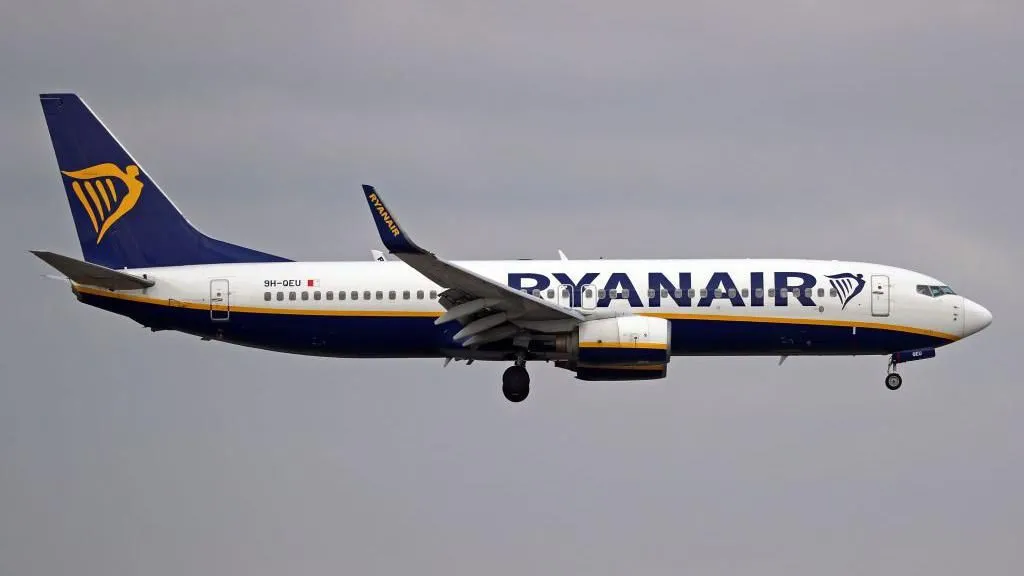 Getty Images ⁤A Ryanair plane in ​the air with white,blue ​and gold livery