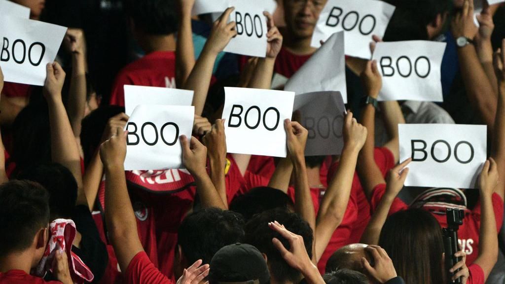 Hong Kong fans turn their backs on the pitch and hold up signs reading 'Boo' while their country's anthem is played