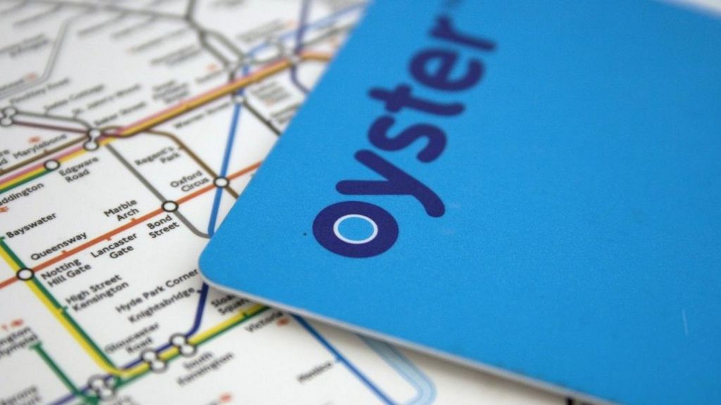 A blue Oyster card is lying over a map of the London Underground with the area around High Street Kensington in focus, with yellow and green circle lines shown on the map