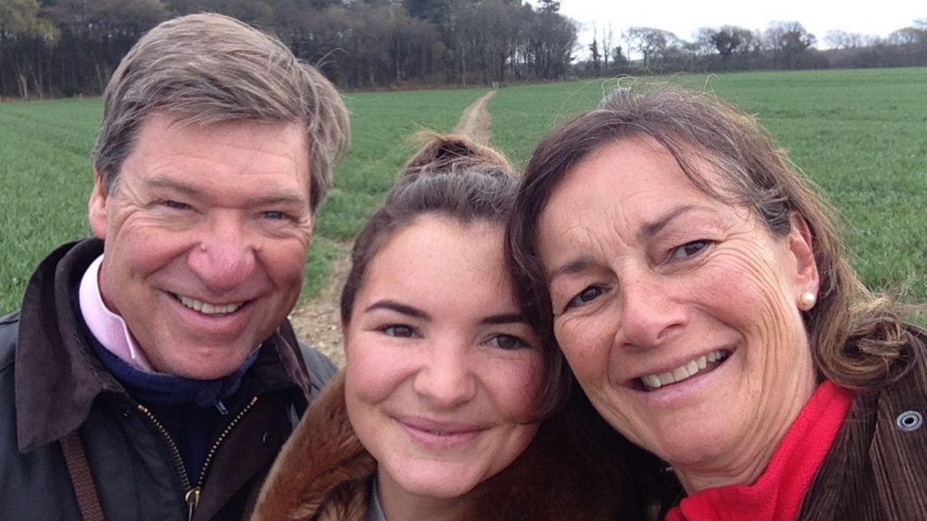 A smiling family take a selfie in a green field. 