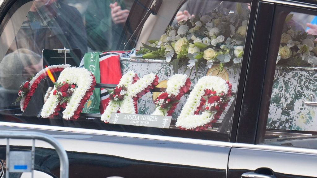 A wreath of flowers reading "R Kid" inside the hearse