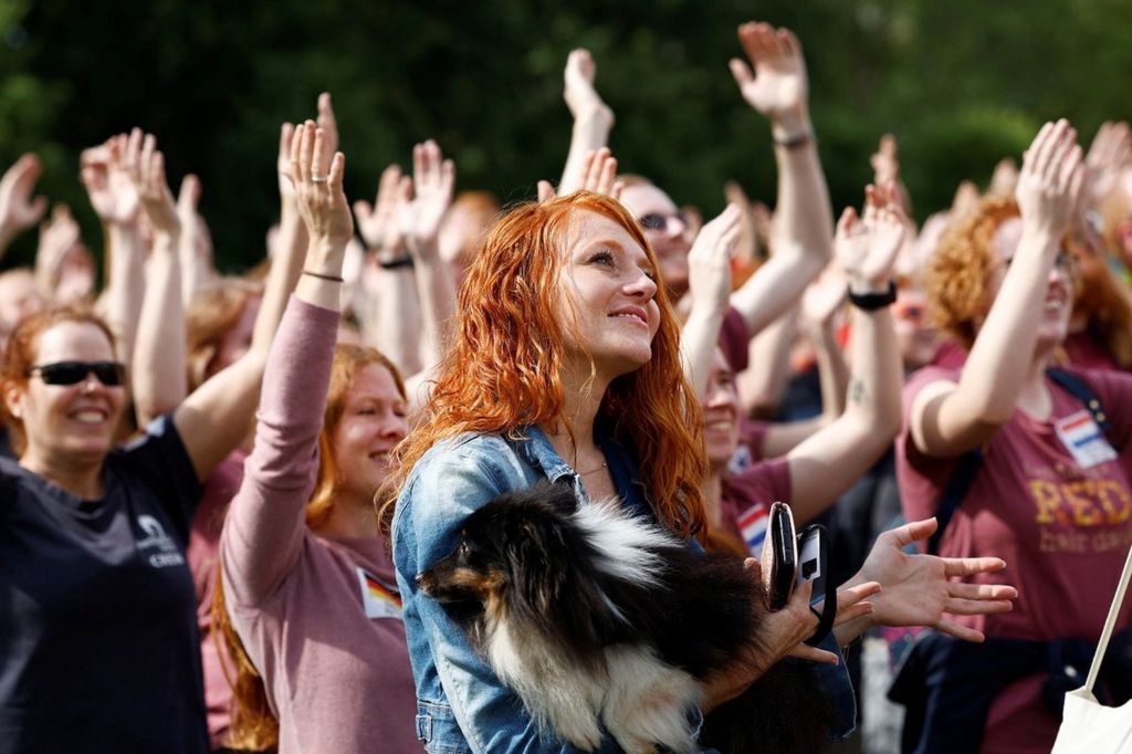 A red-haired woman stands in a crowd with her dog