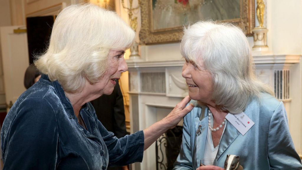 Queen Camilla and Dame Jilly Cooper speaking at a reception at Clarence House, London, in March 2025, and the Queen has one hand on Dame Jilly's shoulder