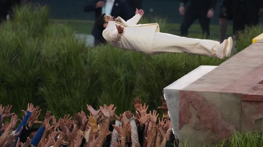 Bad Bunny falls backward from a platform into a crowd of dancers holding up their hands to catch him as he performs at halftime in Super Bowl LX