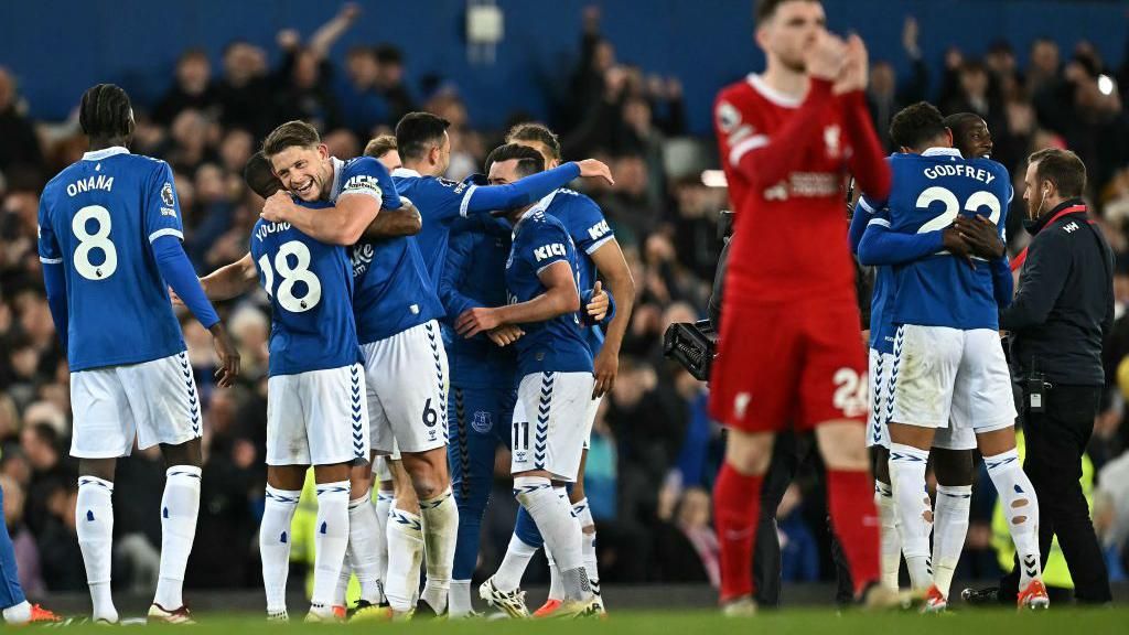 Everton players celebrate together as Andy Robertson claps the away fans in the foreground