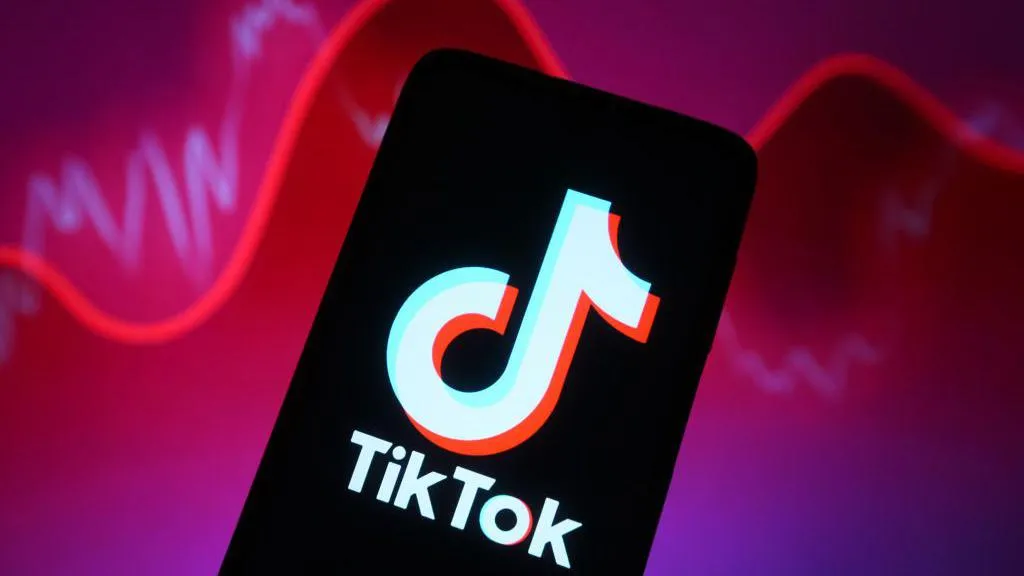TikTok logo shown on a smartphone against a backdrop illustrating rising and falling reports with a red line