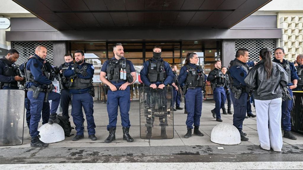 Dozens of French police officers line up outside a store, wearing security vests and with one holding a riot shield.