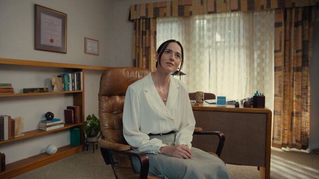 Renate Reinsve in character as therapist Mary. She is sitting wearing a white top and grey skirt