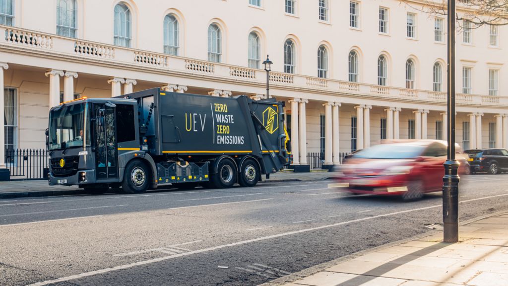 Electric refuse lorry on city road with blurred car in foreground