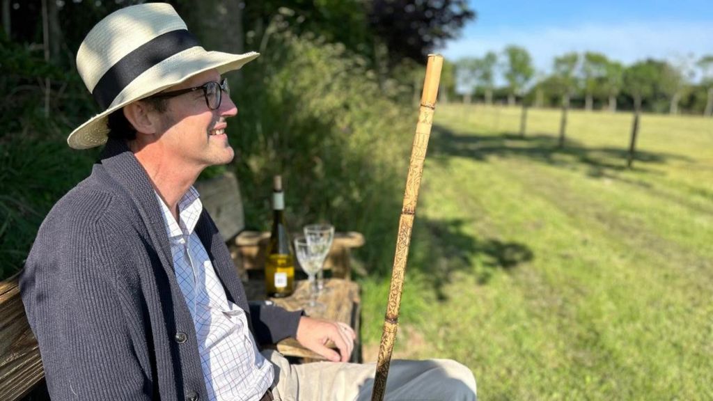 Simon Boas sitting outside looking out on a field, wearing a hat