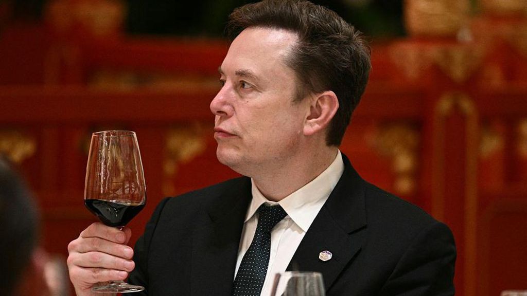 Musk, wearing a black suit, white shirt and black and white dotted tie, holds a glass of red wine while at an event in Beijing, during a recent US trade visit.