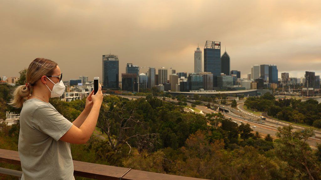 A local resident takes a panoramic image of the bush fire and Perth CBD on her phone from Kings Park on 2 February 2021 in Perth, Australia.